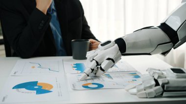Bir robot el, teknoloji ve işyeri verimliliğinin kesişimini gösteren bir insan gözlemlerken grafik ve çizelgeleri içeren iş raporlarıyla meşgul olur. Noogenesis