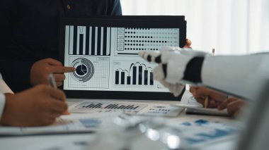 Çeşitli profesyonellerden oluşan bir grup, bir tablet üzerindeki veri eğilimlerinin işbirlikçi bir analizine girişir. Modern ofis ortamında anahtar performans ölçümlerini vurguluyorlar. Noogenesis