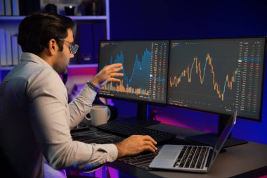 Akıllı tüccar işadamı, karanlık oda gecesinde neon ışıklı ofisteki arama pazarında yüksek kârla ekranda bilgisayar ve bilgisayar üzerinde dinamik borsa yatırımları üzerinde yoğunlaşıyor. Tahmin et..