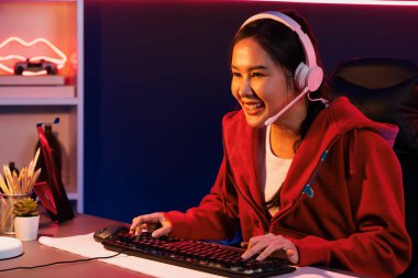 İnternet üzerinden kulaklık takıp gülümseyen Asyalı güzel kız flamasının sunucu kanalı izleyicilerle internet üzerinden konuşma yapıyor. Esport yetenekli takım oyuncuları neon mavi odada. Taktik.