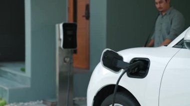 Adamın biri evinde elektrikli araç şarj aletinin fişini çekiyor. İlerici bir yaşam tarzında elektrikli araçların kullanımı, temiz ve sağlıklı bir çevreye katkıda bulunur..