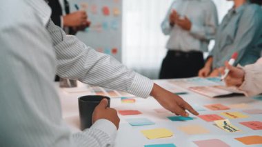 Çeşitli profesyonellerden oluşan bir grup, yapışkan notlar ve modern ofis unsurlarıyla çevrili ve yaratıcılığı ve verimliliği teşvik eden bir takım toplantısı düzenliyor. SACTR