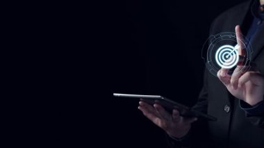 Hedef grafik ve analitik sembollerin yer aldığı dijital pazarlama stratejisini sergileyen bir profesyonel. Bu görüntü, modern iş stratejilerinde veri görselleştirmesinin önemini vurgular. Dörtgen