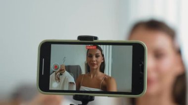 Genç sosyal medyum kadın moda videosu yapıyor. Blogcu kameraya selfie çubuğu ve ışık halkası kullanarak gülümserken, aynı zamanda ikna edici çevrimiçi kıyafetlerin izleyicilere veya takipçilere vlog satmasını sağlıyor. Düzenle