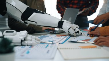 Bir robot el, üretkenliği ve yeniliği artırmak için veri analizi ve strateji geliştirme üzerine odaklanarak, modern ofis ortamında insan ekip üyeleriyle işbirliği yapar.