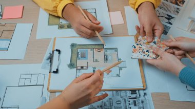 Çeşitli bireylerden oluşan bir grup modern bir çalışma alanında tasarım planları ve çizimler üzerinde işbirliği yapmaktadır. Çeşitli malzemeler ve aletler, takım çalışması ve yaratıcılığın gösterildiği bir masaya dizilmiştir. SACTR