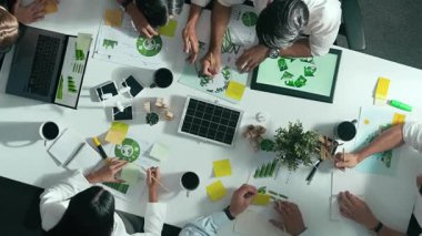 İş adamlarının rüzgar değirmeniyle toplantı masasında temiz enerji ve sürdürülebilir yatırım kullanımı, çevre grafiği ve ahşap ev modeli ile ilgili tartışmalarına tepeden aşağı bakış açısı. Hizalama.