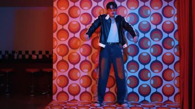 Asyalı break dansçı serbest stile geçiyor ve balon arka planlı kameraya bakıyor. Profesyonel hippi gündelik kıyafet giyer ve gözlük takar. Mutluluk.