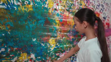 Genç mutlu kız renk tepsisini tutuyor ve fikri ifade etmek ve el iziyle hayal gücünü geliştirmek için renkli duvarları boyuyor. Resim dersinde odayı dekore etmek için beyaz kız pulu. Öğretim