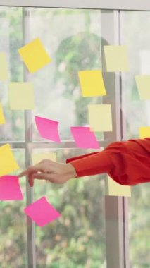 İş adamları ofisteki proje planlama kurulunda çalışıyor ve proje gelişimini analiz etmek için iş arkadaşlarıyla sohbet ediyorlar. Düzenli olması için cam duvara yapıştırılmış yapışkan notlar kullanıyorlar. .