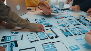Çeşitli bir ekip, mobil arayüz dizaynları ve kablo çerçevelerini analiz ederek yaratıcı bir beyin fırtınası oturumuna katılıyor, yenilik ve işbirliği sergiliyor. SACTR