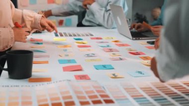 Çeşitli profesyonellerin modern bir çalışma alanı ortamında yapışkan notlar, dizüstü bilgisayarlar ve tartışmalar kullanarak renk paleti oluşturmaya çalıştığı canlı bir işbirliği oturumu. SACTR