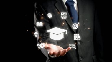 Takım elbiseli bir işadamı, karanlık bir ortamda büyüme, yenilik ve mesleki gelişim fırsatlarını temsil eden çeşitli eğitim ve başarı simgelerini parlak bir şekilde elinde tutuyor. Dörtgen