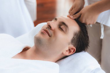 Beyaz adam stres önleyici kafa masajından ve lüks bir tatil beldesi veya otel spa salonundaki modern ışık ortamında yüz güzelliği eğlencelerini şımartmaktan hoşlanıyor. Sessiz.