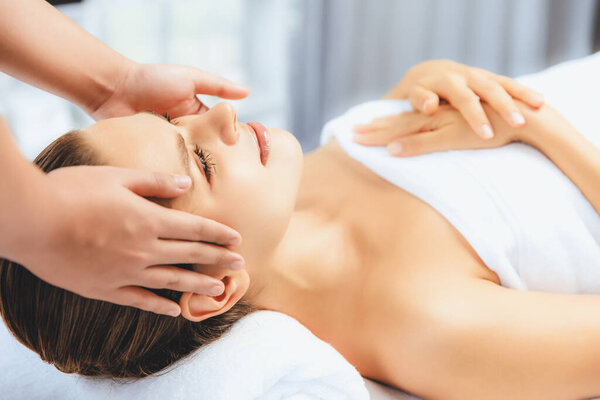 Caucasian woman enjoying relaxing anti-stress head massage and pampering facial beauty skin recreation leisure in dayspa modern light ambient at luxury resort or hotel spa salon. Quiescent
