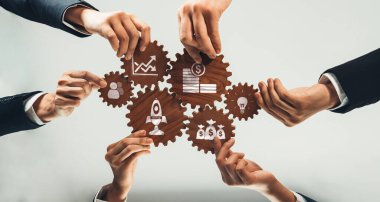 Bir grup farklı el, iş simgelerini içeren vitesleri bağlamak için bir araya geliyor. Bu görüntü takım çalışmasını, yenilikçiliği ve profesyonel bir ortamda başarı arzusunu temsil eder. Dostluk