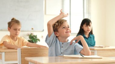 Sınıfta okuyan çeşitli çocuklarla çevrili beyaz bir çocuk öğretmenine soru sorup cevap verdiği için elini kaldırıyor. Mutlu öğrenci birlikte çalışıyor, oy veriyor, gönüllü oluyor, hocayı arıyor. Pedagoji.