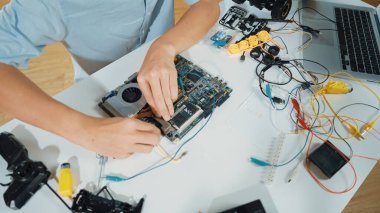 Masadaki elektronik aletle ana kartı tamir eden çocuğa yakın çekim. Elektronik teçhizatla lise öğrencilerinin elektrik panosunun en üst görüntüsü, kablo aletleri masanın etrafına saçılmış. Öğretim.