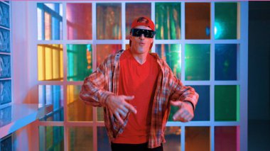 Komik break dansçı kameraya bakarken hiphop 'a doğru serbest adım atıyor. Çılgın mutlu hipster dans edip sokak dansı yaparken Led ışığında günlük kıyafet ve güneş gözlüğü takıyor. Mutluluk.