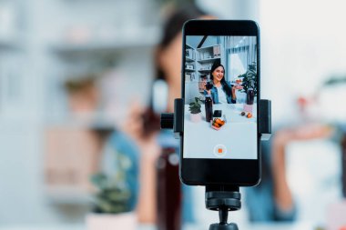 Seçici odaklı akıllı telefon ve gülümseyen genç, güzel Asyalı karışık çilek ve kiraz suyu detoksu değerlendirmesi sosyal medyada sağlıklı ürün tanıtımı sunuyor. Taktik.