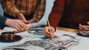 Bir grup mühendis, yenilikçi çözümler geliştirmek için modern bir çalışma alanında teknik çizimler, dişliler ve araçlar kullanarak bir mekanik tasarım projesinde işbirliği yapıyorlar. SACTR