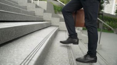 Yakından bakınca iş için çanta tutarken yürüyen zeki bir iş adamının görüntüsü var. Proje yöneticisi çalışmak için merdivenlerden iniyor. Ulaşımı temsil eden, seyahat eden. Bacağa odaklan. Sevinçli..