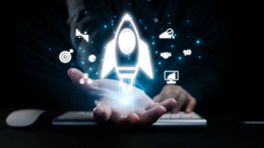 Bir el, yenilik ve büyümeyi simgeleyen, karanlık bir ofis zeminine kurulmuş, teknoloji ve iş gelişiminin yolculuğunu gösteren parlayan bir roket tutuyor. Dörtgen