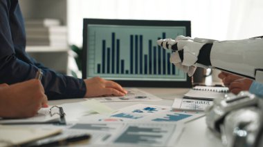 Bir insan ve robotik el iş ortamında etkileşime girer, ekranlardaki veri grafiklerini analiz eder ve modern çalışma ortamlarında karar verme mekanizmasını geliştirir. Noogenesis