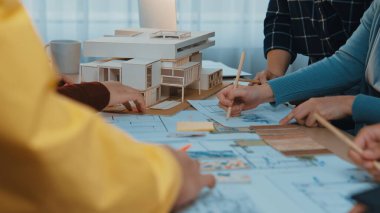 Bir grup mimar bir bina projesinde işbirliği yapıyor, planları tartışıyor ve ayrıntılı bir modeli inceliyor. Sahne, modern bir çalışma alanında yaratıcılığı ve takım çalışmasını yakalıyor. SACTR