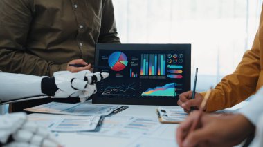 Çeşitli bir ekip modern bir ofiste veri analizi ve içgörüleri tartışarak işbirliği yapıyor. Robot, grafikler ve çizelgeler içeren dijital görüntülerle etkileşime girer.