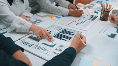 Çeşitli profesyonellerden oluşan bir grup, iş raporları ve veri eğilimlerini analiz eden bir işbirliği oturumunda yer alıyor. Çeşitli grafikler ve grafikler anahtar performans göstergelerini vurguluyor. SACTR