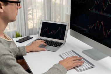 Stresli iş adamı günü modern ofisteki dinamik borsa grafiğine bakıyor, veri tabanı bilgisayarını ve bilgisayarını evden çalışırken karşılaştırıyor. Bireysel.