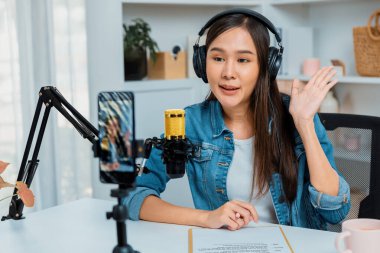 Asyalı sunucu canlı yayında canlı yayında canlı yayında sosyal medyada kulaklık takarak konuşuyor. Dinleyicileri modern stüdyoda koçluk yaparak selamlıyor. Taktik.