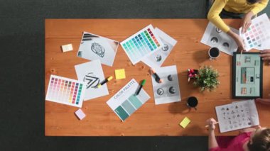 Proje yöneticisi renk paletleri seçerken tasarımcının tablete baktığı yukarıdan aşağıya hava görüntüsü. Profesyonel grafik tasarımının en üst görüntüsü ve logoya bakın. Yetenekli ekip grafikleri seçiyor. Sempozyum.