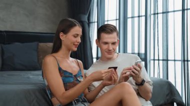 Genç çift, kredi kartıyla ödemek için internet üzerinden ödeme uygulaması ve dijital cüzdan kullanarak yatak odasında oturuyor. Mobil internet üzerinden alışveriş ve modern alımlar. Düzenle