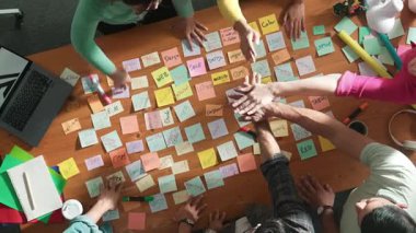 Yapışkan notla toplantıda durup el ele tutuşan tasarımcının yukarıdan görünüşü. Ekibin hava görüntüsü başarılı bir projeyi kutlamak için ya da beyin fırtınası sonrası el ele tutuşur. Sempozyum.