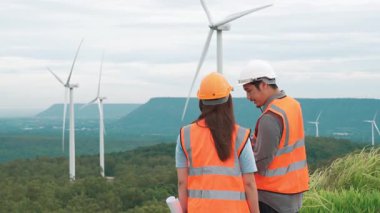 Erkek ve kadın mühendisler kırsal kesimdeki bir tepenin tepesinde ya da dağda rüzgar çiftliğinde çalışıyorlar. Yenilenebilir ve sürdürülebilir enerjinin gelecekteki üretimi için yenilikçi idealler.