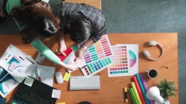 Akıllı tasarımcının renkli paletlerden renk seçmesine yardım ederken yukarıdan aşağı görünümü. Dizüstü bilgisayardan logoya bakarken birlikte çalışan ve planlayan iş adamlarının hava görüntüsü. Sempozyum.