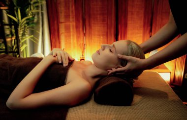 Beyaz kadın stres önleyici kafa masajı yapmaktan ve lüks otel veya otelde sıcak mum ışığında yüz güzelliği eğlencesi yapmaktan zevk alıyor. Sessiz.