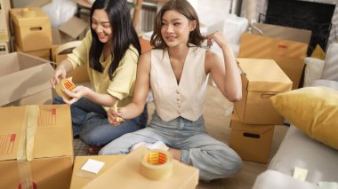 Çekici bir oda arkadaşı oturma odasında paket paketlerken pakette konum yazıyor. Mutlu satıcı birlikte çalışıyor ve teslimat paketini hazırlıyor. Girişimci kargo kutusu paketliyor. Myrmidon.