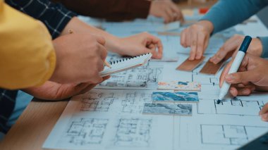 Değişik ellerin, büyük bir masanın üzerine çizimler, planlar ve notlar içeren ortak bir tasarım oturumunda yer aldığını gösteren canlı bir sahne. SACTR