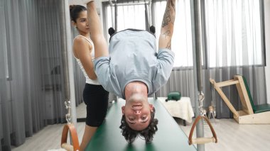 Eğitmen rehberliğinde Pilates Cadillac 'ta ters bacak yükseltme pratiği yapan sağlıklı bir müşteri. Çekirdek dayanıklılığını ve üst vücut dengesini arttırmak için Cadillac 'ı geren adam. Alışkanlık.