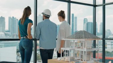 Gökdelene bakıp bir proje planı okurken, günlük kıyafetli akıllı mimar mühendis ekibi konuşuyor. Profesyonel yönetici takımı ev inşaatı hakkında beyin fırtınası yapıyor. Arkadan bak. İzleme