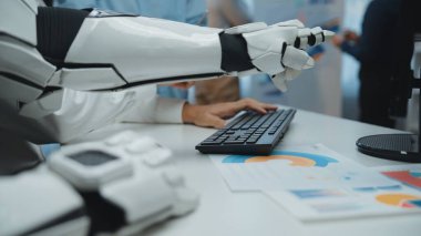 Bir robotik kol masadaki veri grafiklerine işaret eder, modern çalışma alanındaki teknolojiyi vurgular, iş ortamlarında analiz ve yenilik vurgular. Noogenesis