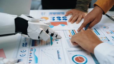 Bir robot el ve insan eli stratejik bir iş toplantısı sırasında çeşitli veri tabloları ve gösterge tablolarının ortak analizini yapar. Noogenesis