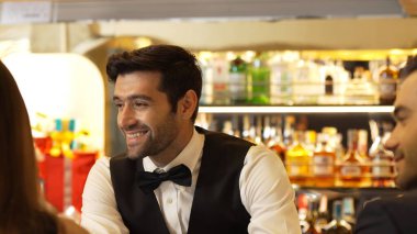 Güzel görünümlü barmen, içki tezgahındaki çiftle samimi bir gülümseme sohbeti yaparken aynı zamanda hoş geldin içkisi ve özel menü listesi öneren çekici profesyonellik. Vinosity.