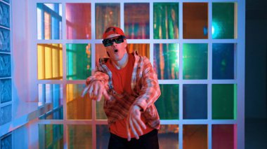 Komik break dansçı kameraya bakarken hiphop 'a doğru serbest adım atıyor. Çılgın mutlu hipster dans edip sokak dansı yaparken Led ışığında günlük kıyafet ve güneş gözlüğü takıyor. Mutluluk.