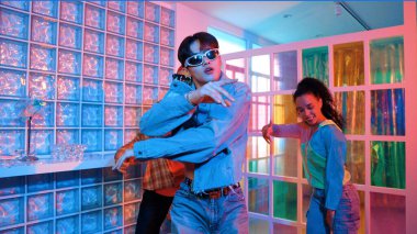 Asyalı adam gece kulübünde çeşitli neon ışıklarda dans ederken kolunu oynatıyor. Modern kulüpte çok kültürlü hippilerle dans eden şık elbiseli mutlu dansçı. Mutluluk.