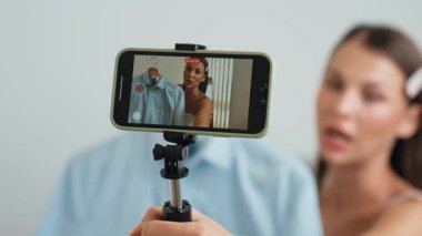 Genç sosyal medyum kadın moda videosu yapıyor. Blogcu kameraya selfie çubuğu ve ışık halkası kullanarak gülümserken, aynı zamanda ikna edici çevrimiçi kıyafetlerin izleyicilere veya takipçilere vlog satmasını sağlıyor. Düzenle