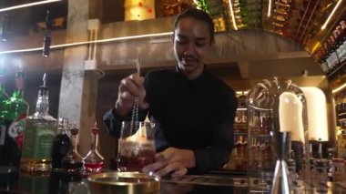 Zeki Asyalı barmen bardakta karıştırılmış alkol şurubunu buzla karıştırıyor. Çünkü kayanın üzerinde kamera var. Gece kulübünde taze kokteyl kokteylleri karıştırıyor. Vinosity.